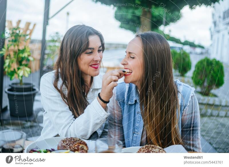 Junge Frau, die ihren Freund in einem Straßenrestaurant füttert essen essend Freundinnen Strassenrestaurants Straßenrestaurants Freunde Freundschaft