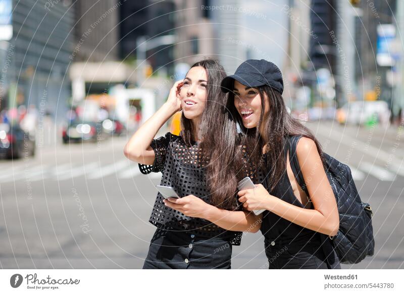 USA, New York City, zwei glückliche Zwillingsschwestern mit Mobiltelefonen in Manhattan Schwester Schwestern Handy Handies Handys New York State Spaß Spass
