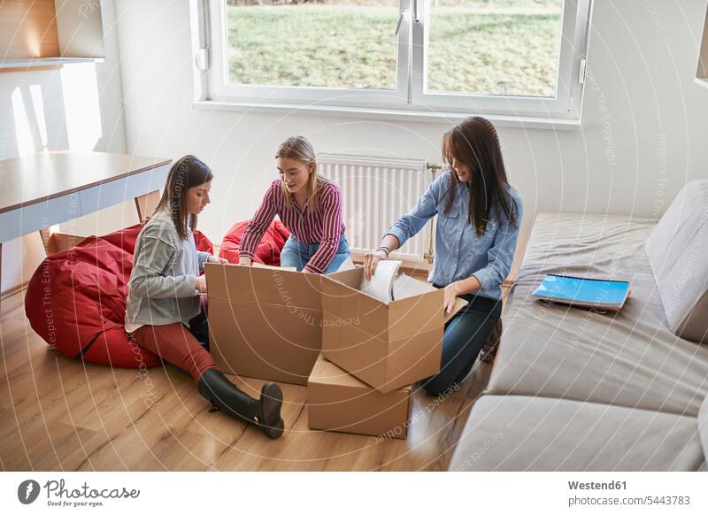 Drei junge Frauen packen in einem Raum Pappkartons aus weiblich Freundinnen Zimmer Räume auspacken Karton Kartons Erwachsener erwachsen Mensch Menschen Leute