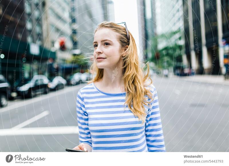 USA, New York, Manhattan, Junge Frau, die auf der Straße geht und ein Mobiltelefon in der Hand hält weiblich Frauen blond blonde Haare blondes Haar jung