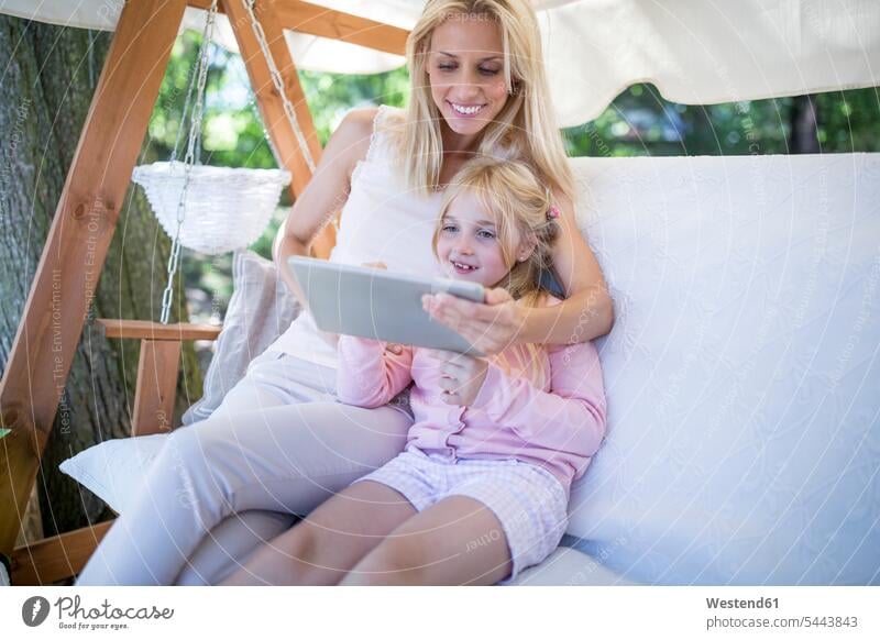 Lächelnde Mutter und Tochter sitzen im Baldachin und schaukeln mit dem Tabet Mami Mutti Mütter Mama Töchter lächeln Hollywoodschaukel Tablet Tablet Computer