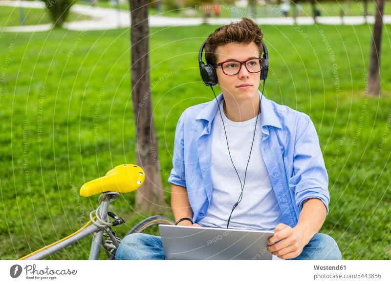 Porträt eines seriösen jungen Mannes mit Rennrad, der mit Laptop und Kopfhörer auf einer Bank sitzt Männer männlich Kopfhoerer Notebook Laptops Notebooks