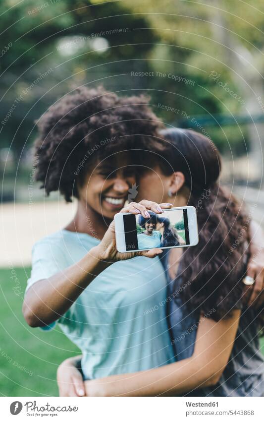Zwei Frauen, die sich mit ihrem Smartphone in einem Park fotografieren iPhone Smartphones Paar Pärchen Paare Partnerschaft Selfie Selfies Handy Mobiltelefon