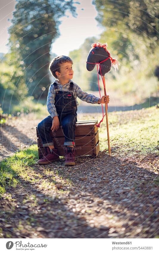 Junge mit einem Steckenpferd auf Holzkiste sitzend Fantasie Phantasie Spielzeugpferd Kindheit sitzt spielen Buben Knabe Jungen Knaben männlich Kinder Kids