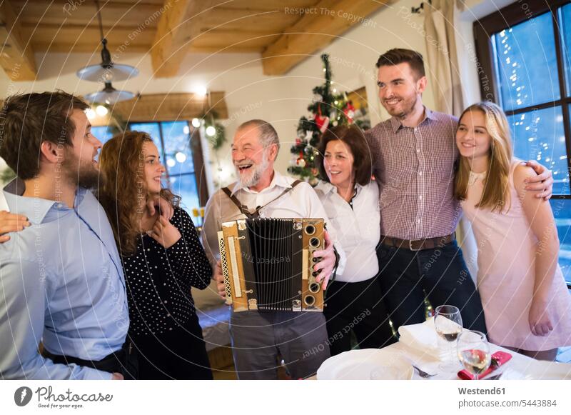 Älterer Mann spielt zu Weihnachten Akkordeon für glückliche Familie Spaß Spass Späße spassig Spässe spaßig Christmas X-Mas X mas feiern Party Parties Partys