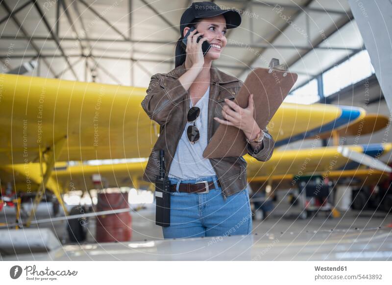 Weibliche Pilotin telefoniert im Hangar inspizieren prüfen Flugzeug Flieger Flugzeuge telefonieren anrufen Anruf telephonieren überprüfen testen checken Handy