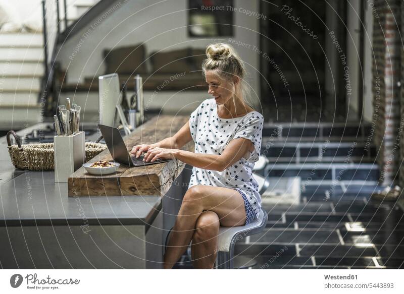 Frau sitzt in der Küche und benutzt Laptop Notebook Laptops Notebooks weiblich Frauen Zuhause zu Hause daheim morgens Morgen früh Frühe arbeiten Arbeit sitzen