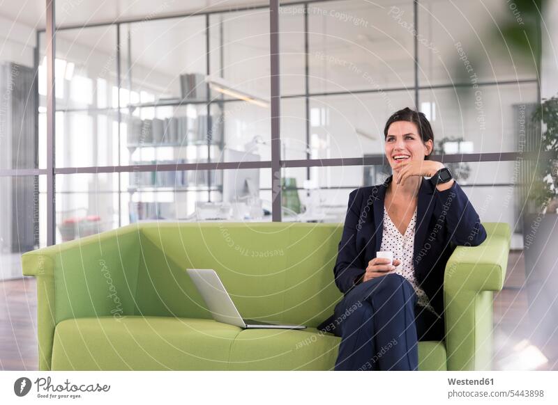 Geschäftsfrau mit Laptop, die auf einer Couch sitzt und im Büro Kaffee trinkt Smartwatch arbeiten Arbeit Internet Laptop benutzen Laptop benützen Unabhängigkeit