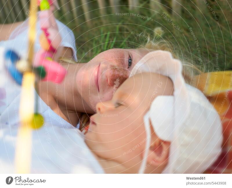 Lächelndes Mädchen liegt mit Baby auf Decke auf einer Wiese weibliche Babys weibliches Baby weibliche Babies Kind Kinder Mensch Menschen Leute People Personen