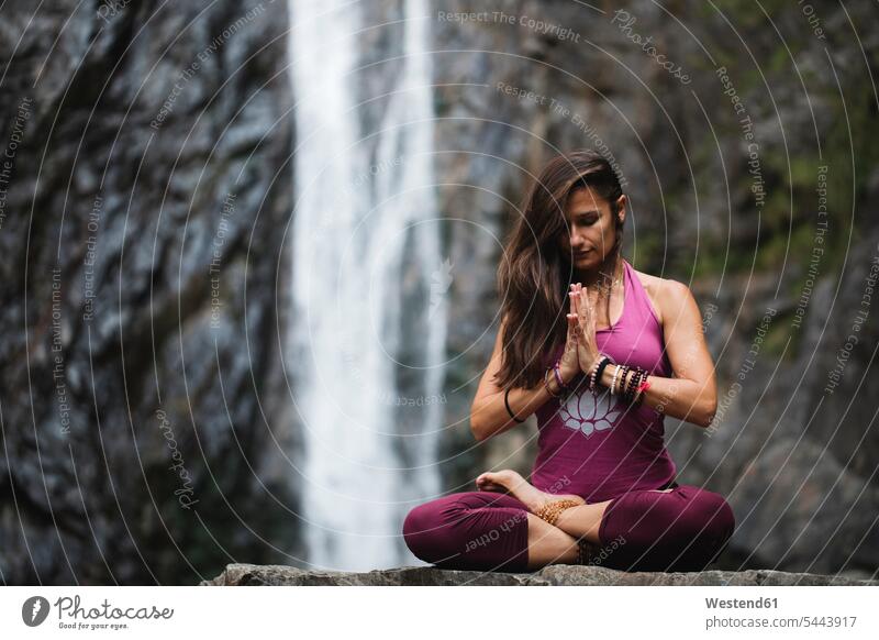 Italien, Lecco, Frau beim Meditieren in der Nähe eines Wasserfalls Wasserfälle Wasserfaelle sitzen sitzend sitzt Meditation meditieren Yoga Yoga-Übungen