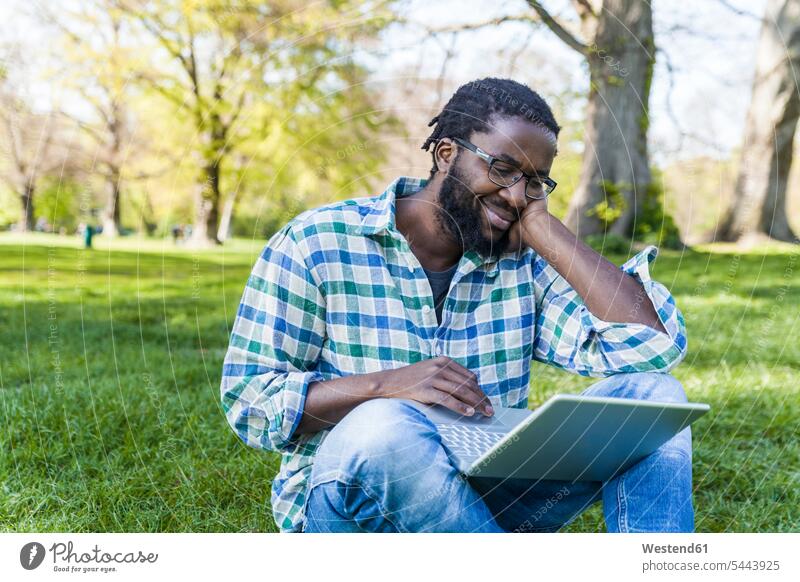 Zufriedener Mann sitzt mit Laptop auf einer Wiese Notebook Laptops Notebooks Männer männlich Computer Rechner Erwachsener erwachsen Mensch Menschen Leute People