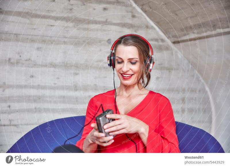 Lächelnde Frau sitzt auf Stuhl und hört Musik vom Walkman Kopfhörer Kopfhoerer weiblich Frauen sitzen sitzend lächeln hören hoeren Erwachsener erwachsen Mensch