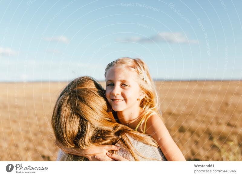 Porträt einer lächelnden Tochter, die ihre Mutter auf einem Feld umarmt umarmen Umarmung Umarmungen Arm umlegen Mami Mutti Mütter Mama Töchter Felder Eltern