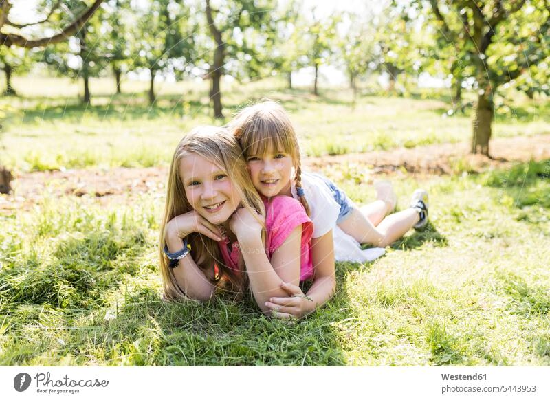 Zwei lächelnde Schwestern liegen auf der Wiese liegend liegt glücklich Glück glücklich sein glücklichsein Wiesen Garten Gärten Gaerten Mädchen weiblich