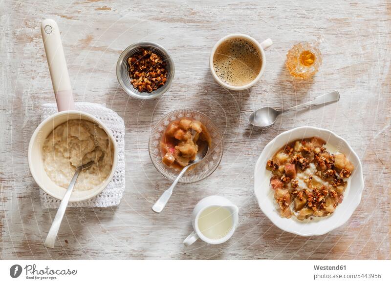 Frühstück mit einer Schüssel Haferbrei mit Rhabarberkompott, Honig und Nüssen und einer Tasse Kaffee Zutaten servierfertig angerichtet Schalen Schälchen
