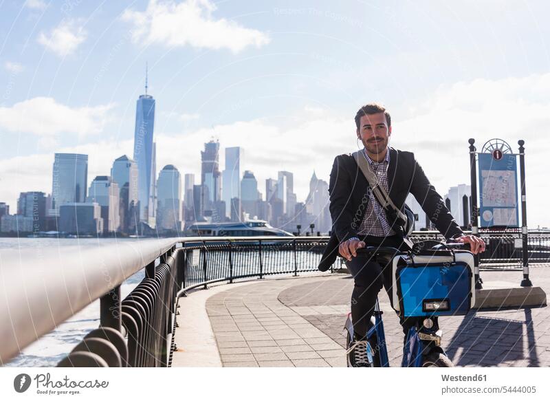 USA, Mann auf dem Fahrrad am Hafen von New Jersey mit Blick auf Manhattan Geschäftsmann Businessmann Businessmänner Geschäftsmänner fahren fahrend fahrender