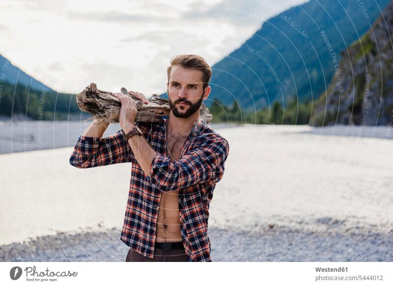 Deutschland, Bayern, Porträt eines jungen Mannes, der in der Natur Brennholz auf seiner Schulter trägt Männer männlich Portrait Porträts Portraits Erwachsener