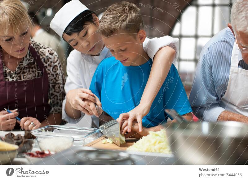 Köchin unterweist Jungen im Kochkurs Küche schneiden kochen Gruppe Gastronomie Mensch Gemeinsam Fürsorge Zubereitung Teilnehmer Wissen fünf Personen Küchenbrett
