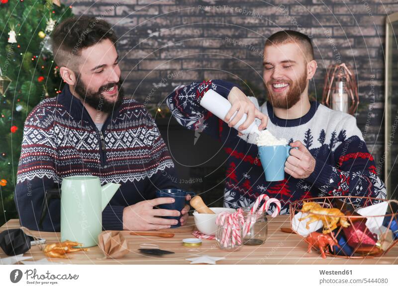 Schwules Paar bereitet zur Weihnachtszeit heiße Schokolade mit Sahne und gehackten Zuckerstangen zu Weihnachten Christmas X-Mas X mas Schwuler Feste Festtag