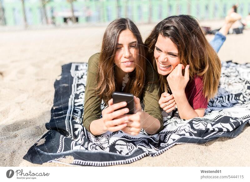 Zwei glückliche Freundinnen telefonieren am Strand Handy Mobiltelefon Handies Handys Mobiltelefone Spaß Spass Späße spassig Spässe spaßig Beach Straende Strände
