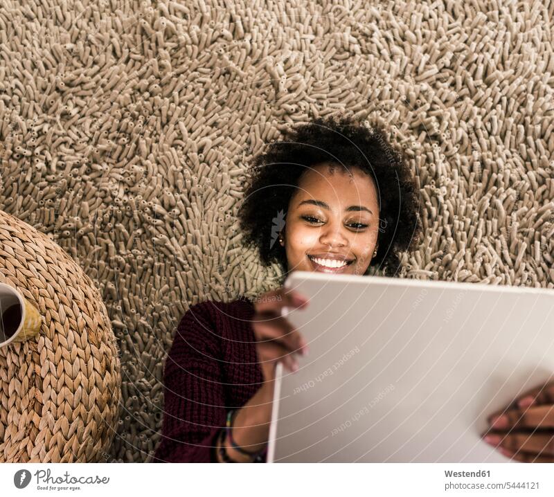 Lächelnde junge Frau mit Tablette auf Teppich liegend Tablet Computer Tablet-PC Tablet PC iPad Tablet-Computer lächeln entspannt entspanntheit relaxt weiblich