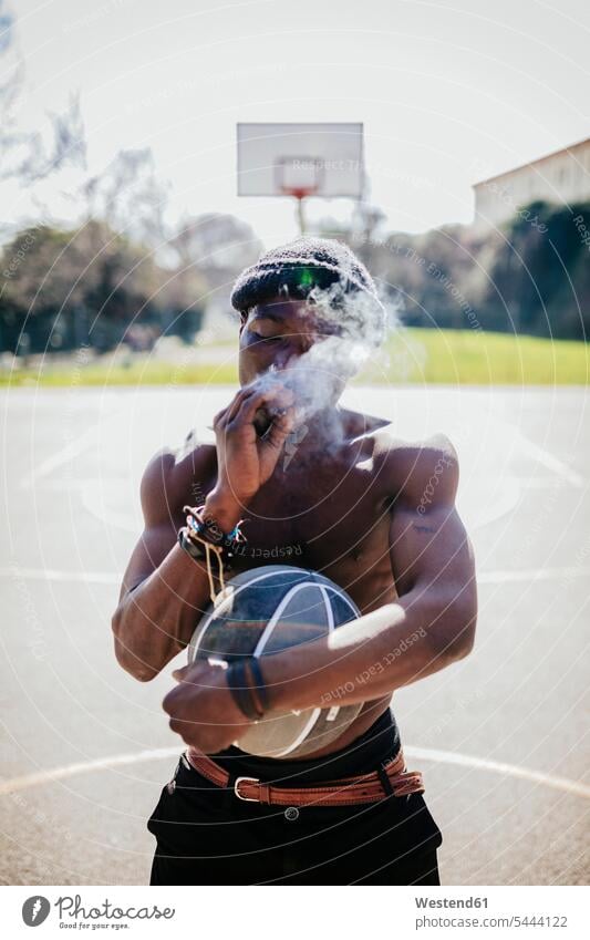 Barbusiger Basketballspieler auf dem Platz, der einen Joint raucht Mann Männer männlich Basketbaelle Basketbälle Basketballer rauchen Erwachsener erwachsen