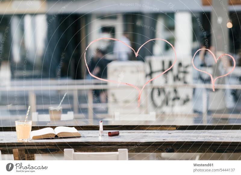 Buch und Getränk in einem Café mit auf Fenster gemalten Lippenstiftherzen Cafe Kaffeehaus Bistro Cafes Cafés Kaffeehäuser Bücher Gastronomie Innenaufnahme