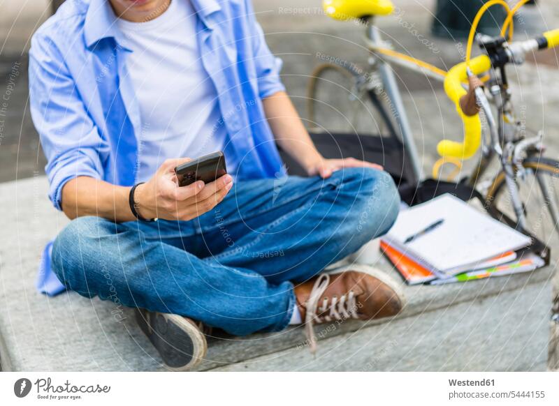 Junger Mann mit Rennrad sitzt auf Bank und benutzt Handy Smartphone iPhone Smartphones Hände Mobiltelefon Handies Handys Mobiltelefone Telefon Kommunikation