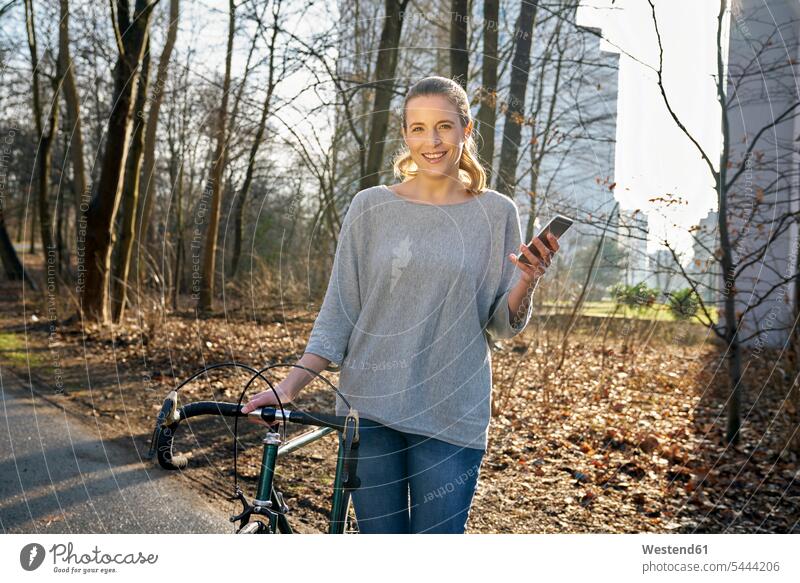 Porträt einer lächelnden blonden Frau mit Rennrad und Mobiltelefon Portrait Porträts Portraits weiblich Frauen Erwachsener erwachsen Mensch Menschen Leute