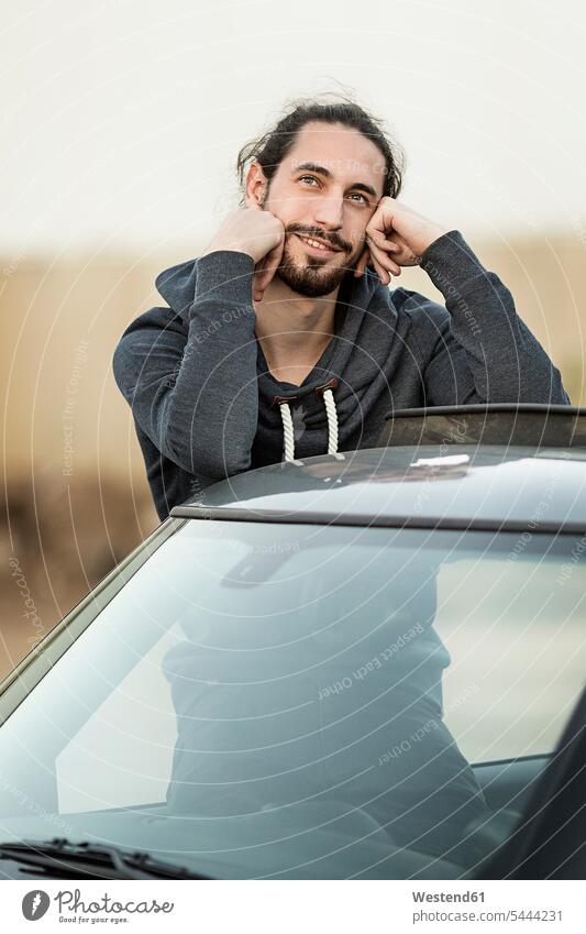 Porträt eines tagträumenden jungen Mannes, der sich auf dem Dach seines Autos anlehnt Männer männlich Portrait Porträts Portraits Wagen PKWs Automobil