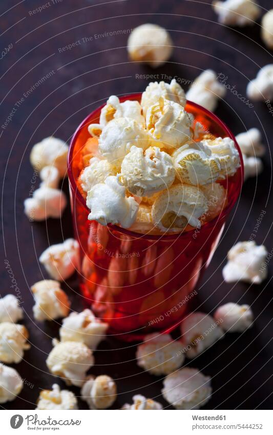 Roter Plastikbecher mit Popcorn Kunststoff glänzend glaenzend Glanz zubereitet Knabberei Knabbereien Mais servierfertig angerichtet verstreut