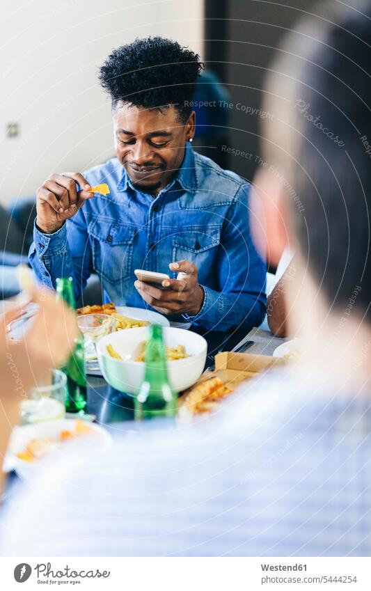 Lächelnder Mann schaut auf Handy am Esstisch Tisch Tische essen essend lächeln Mobiltelefon Handies Handys Mobiltelefone Telefon telefonieren Kommunikation