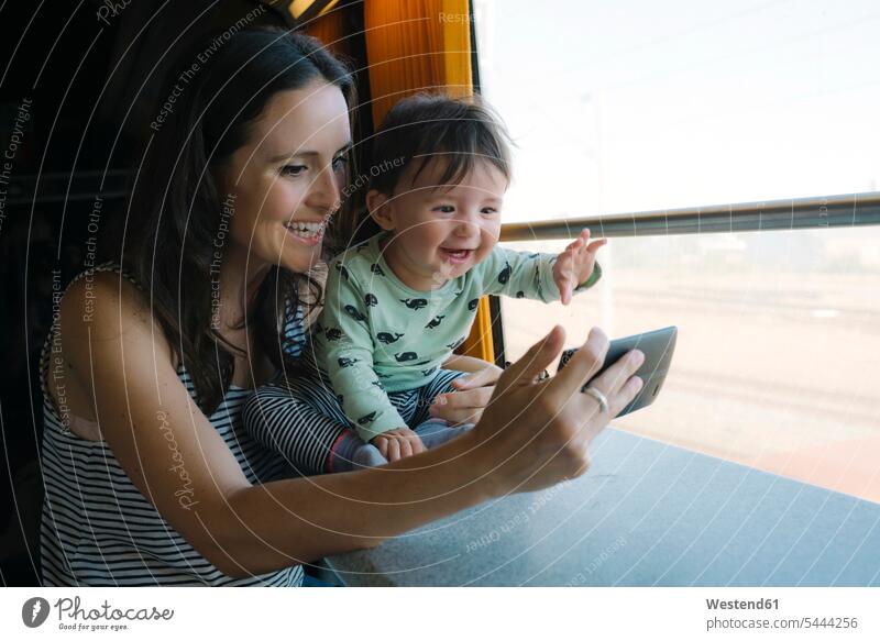 Glückliche Mutter und kleines Mädchen benutzen Smartphone während der Zugfahrt Mami Mutti Mütter Mama reisen verreisen Handy Mobiltelefon Handies Handys