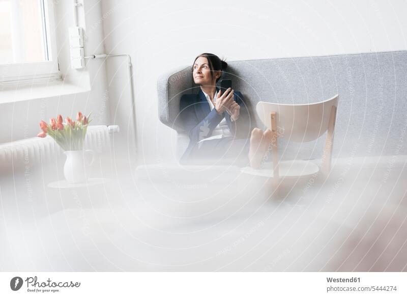 Geschäftsfrau, die auf einer Couch in einem Loft sitzt und aus dem Fenster schaut Frau weiblich Frauen Geschäftsfrauen Businesswomen Businessfrauen