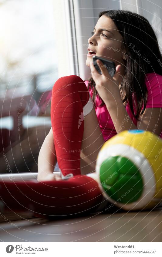 Mädchen im Fussball-Outfit sitzt auf dem Boden im Wohnzimmer und spricht mit jemandem über ihr Smartphone sprechen reden Handy Mobiltelefon Handies Handys