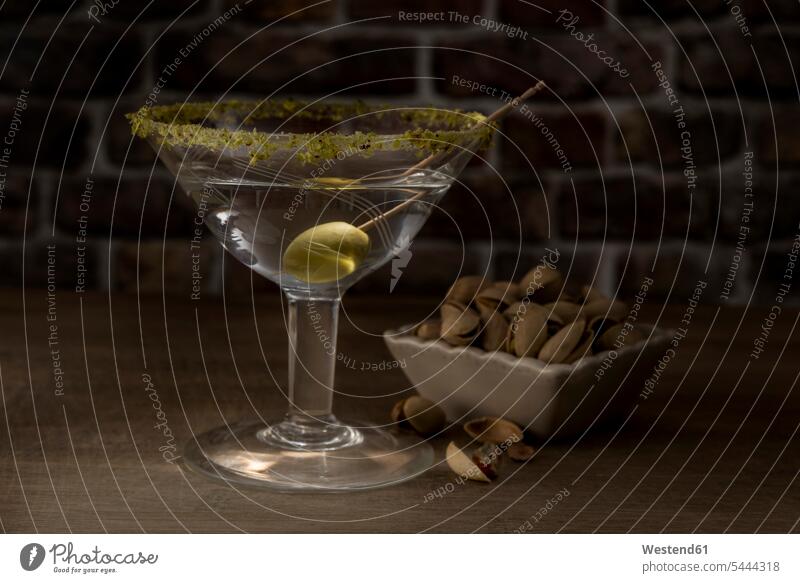 Trockener Martini mit grüner Olive und Pistazie trinken Genuss genießen Genuß geniessen Lifestyle Lebensstil hölzern angerichtet garniert Zahnstocher