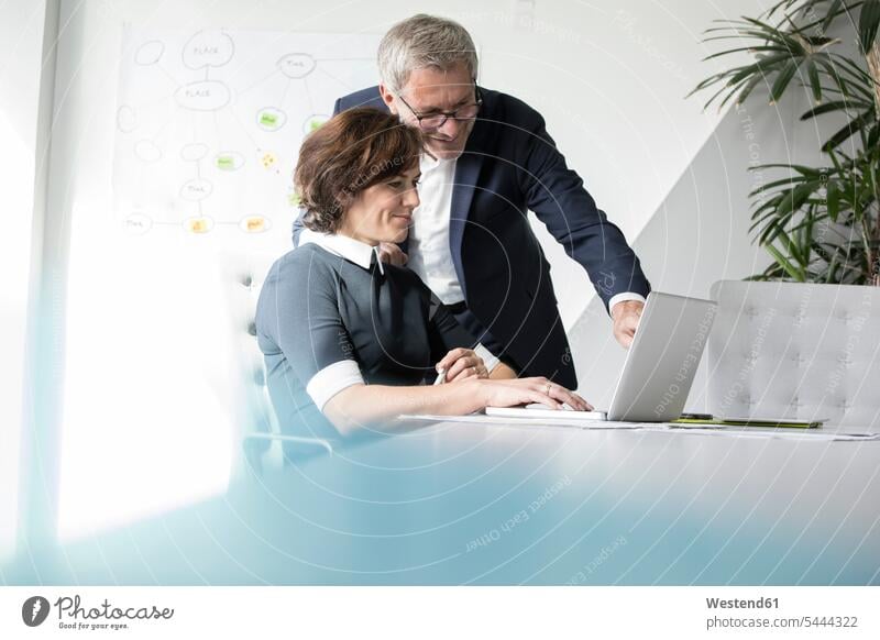 Geschäftsmann und Geschäftsfrau benutzen gemeinsam einen Laptop im Büro lächeln Kollegen Arbeitskollegen Notebook Laptops Notebooks Computer Rechner sprechen