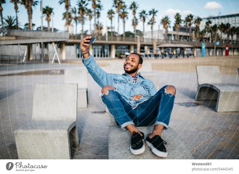 Spanien, Barcelona, lächelnder junger Mann macht Selfie auf der Strandpromenade Selfies Männer männlich Strandpromenaden Erwachsener erwachsen Mensch Menschen