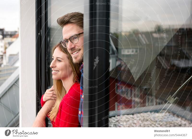 Lächelndes junges Paar schaut aus dem Fenster schauen sehend Zuhause zu Hause daheim Pärchen Paare Partnerschaft lächeln Mensch Menschen Leute People Personen