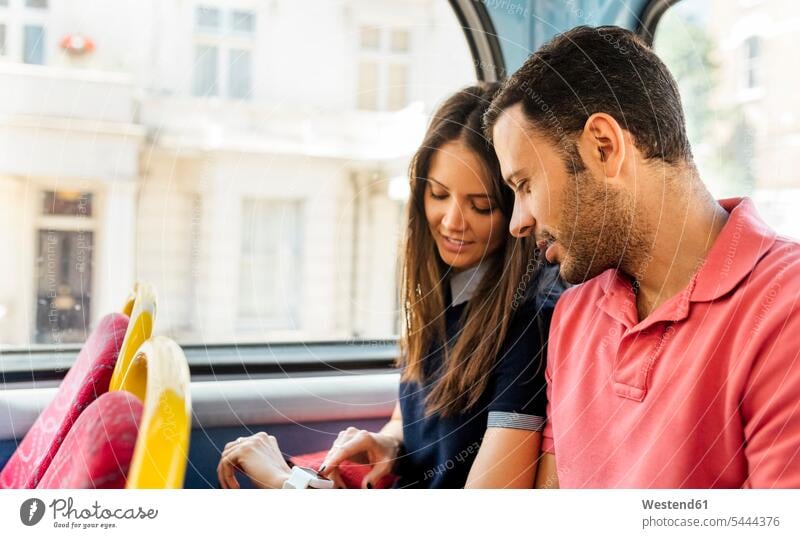Großbritannien, London, Ehepaar sitzt in einem Doppeldeckerbus und nutzt Smartwatch Paar Pärchen Paare Partnerschaft Mensch Menschen Leute People Personen Bus