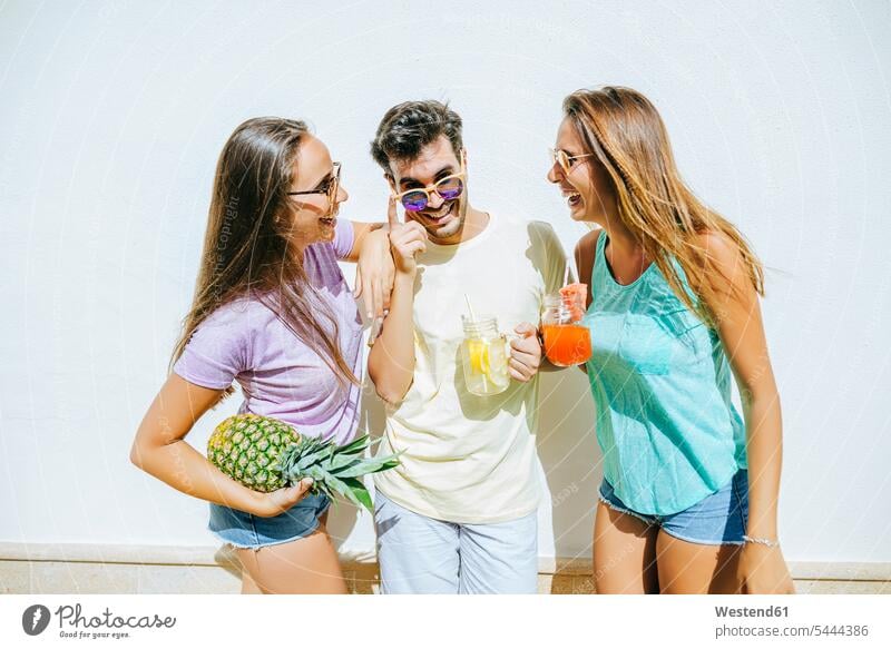 Glückliche Freunde halten erfrischende Getränke und Ananas vor der weißen Wand lachen glücklich glücklich sein glücklichsein Getraenk Getraenke positiv Emotion