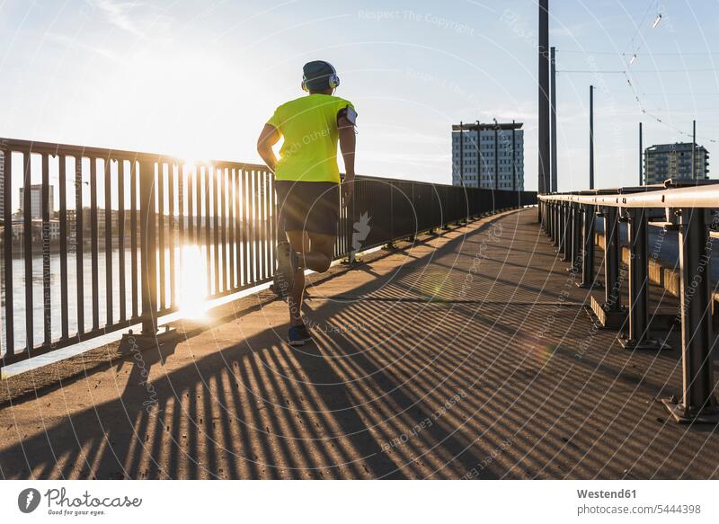 Junger Athlet beim Joggen auf einer Brücke in der Stadt Mann Männer männlich laufen rennen Kopfhörer Kopfhoerer Bruecken Brücken Jogger Sportler fit sportlich