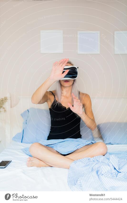 Junge Frau sitzt im Bett und trägt eine VR-Brille Brillen Virtuelle Realität Virtuelle Realitaet weiblich Frauen Betten sitzen sitzend Erwachsener erwachsen