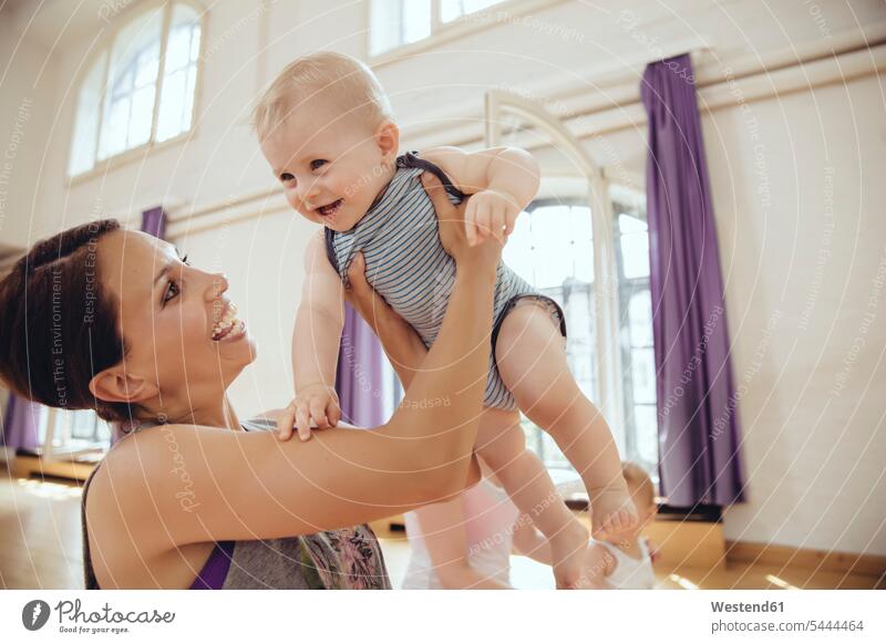 Glückliche Mutter hebt ihr Baby in einem Übungsraum hoch trainieren Spaß Spass Späße spassig Spässe spaßig Mami Mutti Mütter Mama Babies Babys Säuglinge Kind