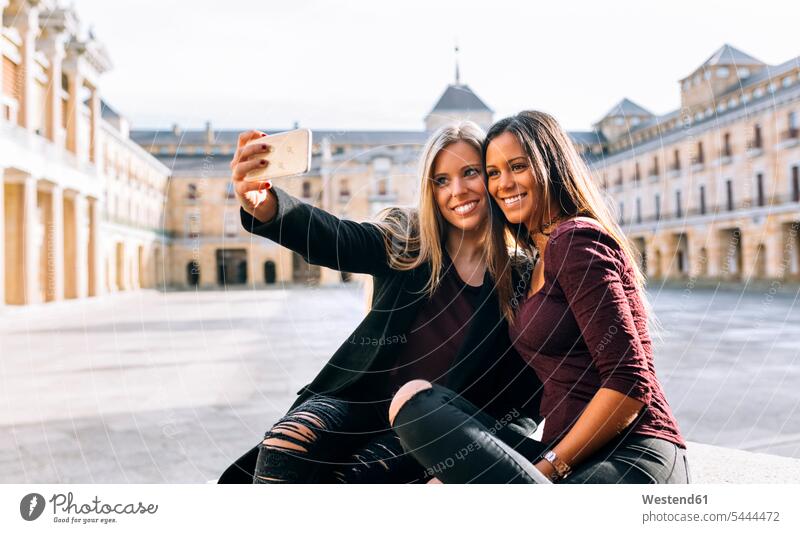 Zwei lächelnde junge Frauen auf einem städtischen Platz machen ein Selfie Handy Mobiltelefon Handies Handys Mobiltelefone Selfies weiblich Freundinnen