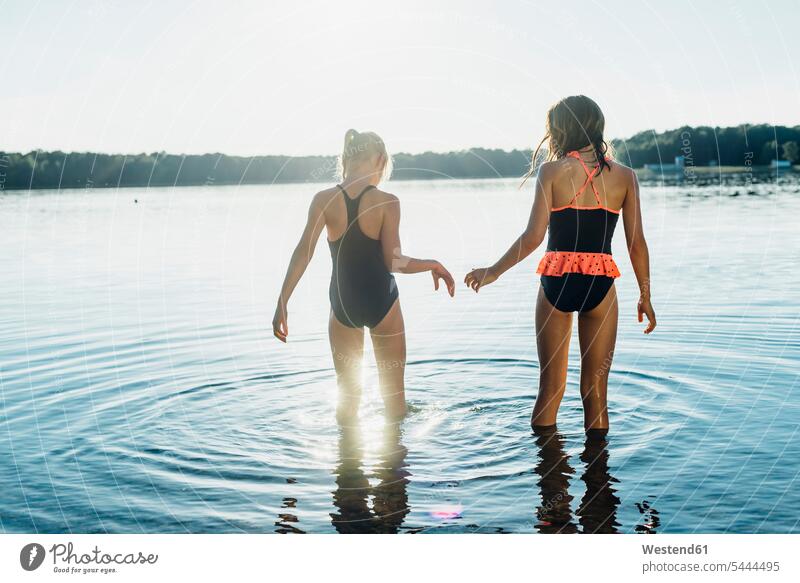 Rückenansicht von zwei Freunden in Badeanzügen am Seeufer stehend Mädchen weiblich Freundinnen Seen Kind Kinder Kids Mensch Menschen Leute People Personen