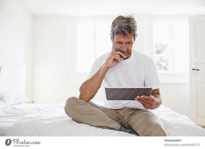 Porträt eines reifen Mannes mit digitalem Tablett im Schlafzimmer Männer männlich lesen Lektüre sitzen sitzend sitzt Tablet Computer Tablet-PC Tablet PC iPad