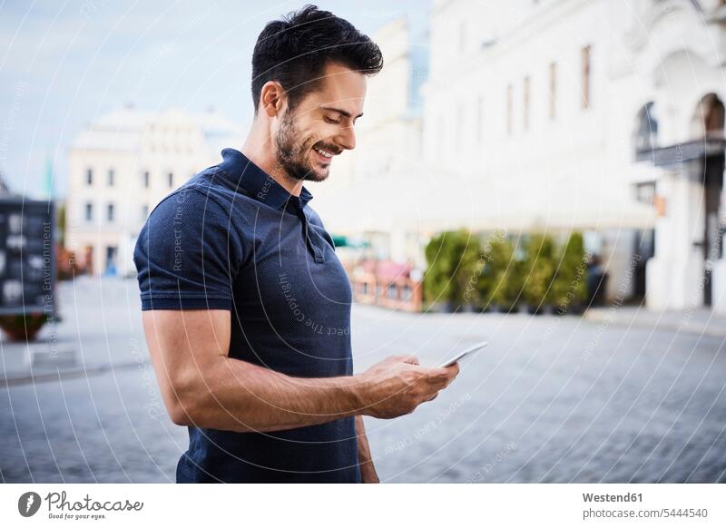 Lächelnder Mann benutzt Handy in der Stadt glücklich Glück glücklich sein glücklichsein Männer männlich Mobiltelefon Handies Handys Mobiltelefone lächeln