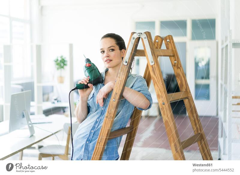 Porträt einer Frau an einer Leiter, die eine elektrische Bohrmaschine hält Umzug umziehen Portrait Porträts Portraits Schlagbohrer Bohrer Bohrmaschinen weiblich