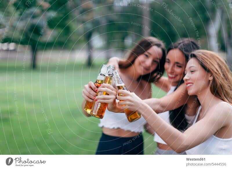 Freunde im Park klirren an Bierflaschen halten anstoßen zuprosten anstossen Freundinnen Parkanlagen Parks Alkohol Alkoholische Getraenke Alkoholisches Getränk